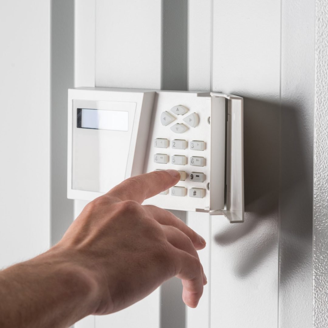 person typing on keypad of home security alarm, security system concept